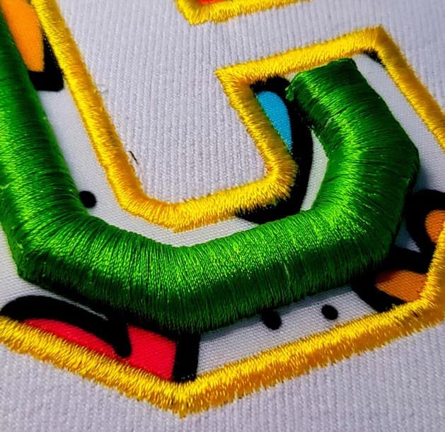 Close-up of green 3D puff-style embroidery lettering with raised details, yellow outlines, and black and red accents.